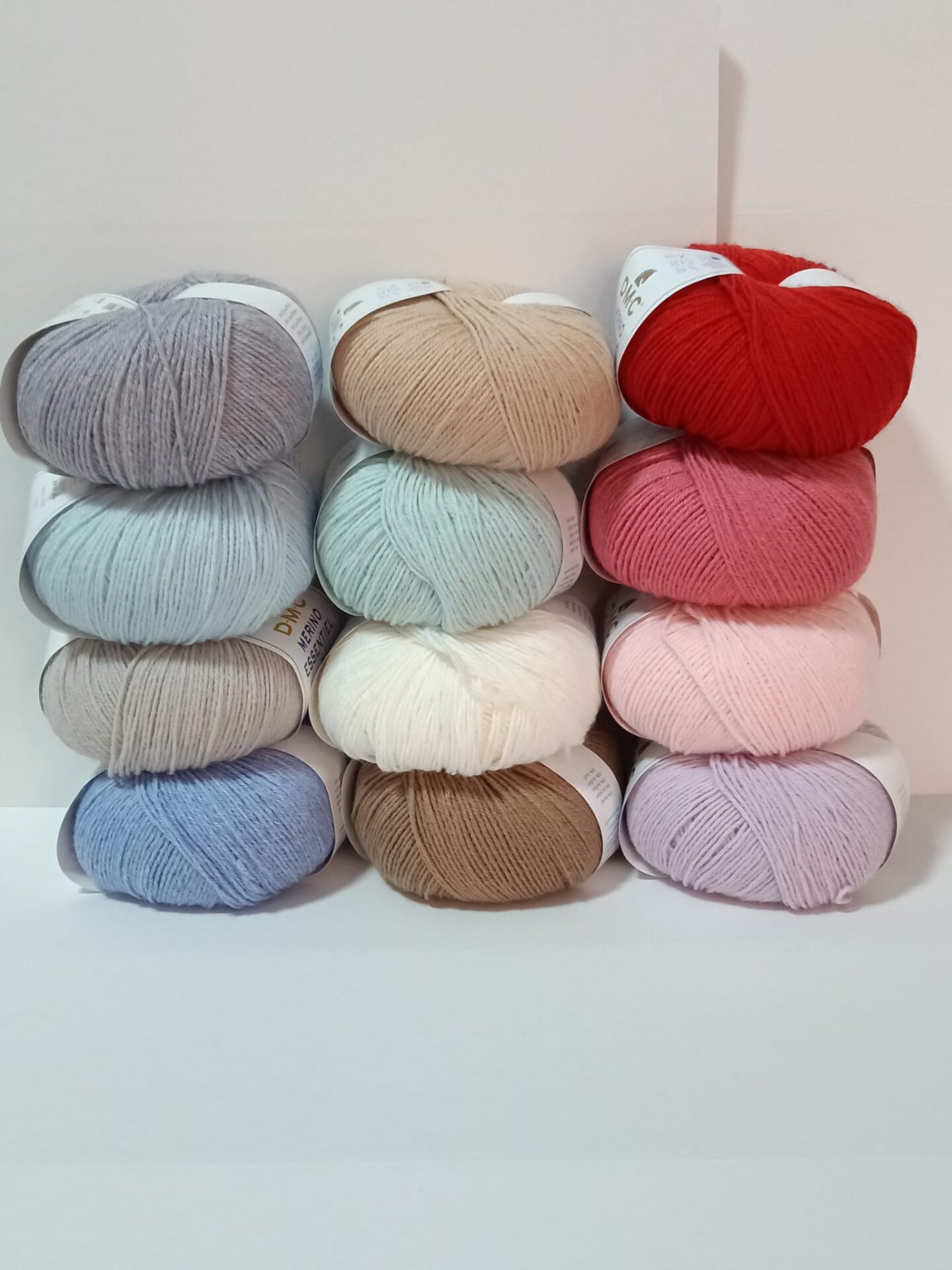 Pila de doce ovillos lana colores etiqueta dmc merino essentiel 3 soft light pure wool blend